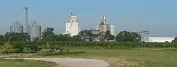 Metal and concrete grain bins and elevators; cornfield in foreground