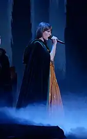 Taylor Swift performing, dressed in a black hood and orange dress