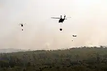 Photograph of three helicopters carrying buckets of water over a burning forest