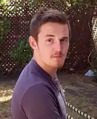 A man in a purple shirt is seen turning his head, facing the direction of the image