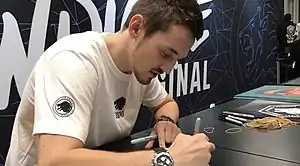 A man is signing a poster on a black table with accessories at a convention