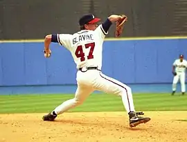 A left-handed baseball pitcher wearing a black baseball cap, white uniform, and black shoes; the back of his uniform has the lettering "GLAVINE" and the number 47, in a throwing stance.