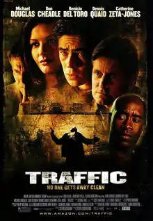 Film poster with five people shown from the neck up. The man on the left has his pointer finger pressed against his lips; the woman to his right has long hair and is smiling; the three man at the right have grim looks as they stare to the right. Below them are several vehicles and a man holding a gun that is getting shot. The top of the image includes the starring credits, while the bottom includes the title of the film and the main credits.