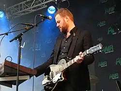 Man playing keyboard while holding a guitar