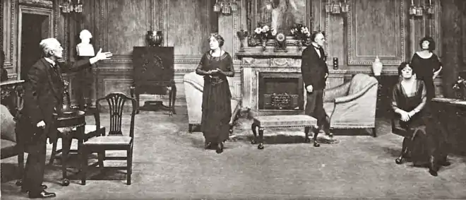 stage indoor scene: three men and two women in discussion, with some gesticulation