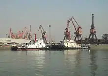 two black and white tugboats berthed against a background of large cranes