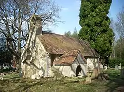 A simple chapel with a bellcote and a protruding porch, and winter trees behind
