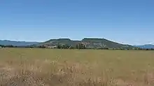 Upper Table Rock from across a field of grass, looking into the central bowl. It rises steeply from the surrounding valley to its flat top.