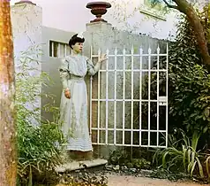Italian woman in formal dress, posed, standing near gate, circa 1905–1915