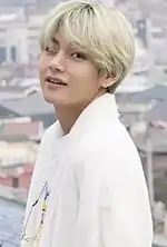 V, in all white, smiles and faces left
