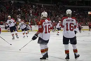 Canadian male in white uniform and white helmet standing next to European male also in white uniform and helmet