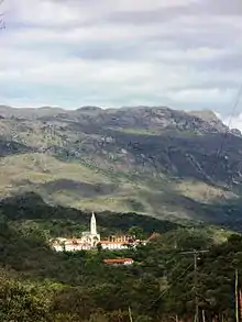 Building with tall spire nestled at the foot of a mountain range in the background