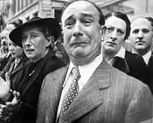 A Freshman in front of a well dressed crowd crying while appearing to be suppressing his emotions by pressing his lips and contorting his forehead