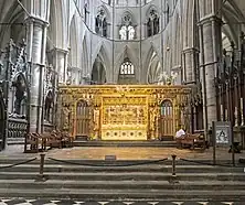 A golden altar and screen in the centre of a grey stone church.
