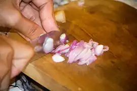 A person chopping shallots for making satay