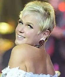 A blue-eyed blond woman with a pixie cut and stud earrings facing to her right.