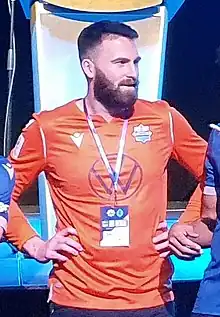 Bearded man in an orange jersey standing straight, hands on his hips