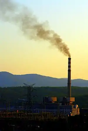 Smoke rising from a tall chimney just after sunset against a background of mountains