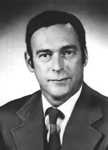 Headshot of a dark-haired, clean-shaven, middle-aged man wearing a suit