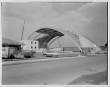 The Island Garden arena construction site in 1956. A large, vaulted frame — reminiscent of an airplane hanger — has half its ceiling assembled.