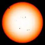 The sun in orange, as seen from the visible spectrum, with Venus in the top left quadrant
