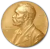 A golden medallion with an embossed image of a bearded man facing left in profile. To the left of the man is the text "ALFR•" then "NOBEL", and on the right, the text (smaller) "NAT•" then "MDCCCXXXIII" above, followed by (smaller) "OB•" then "MDCCCXCVI" below.