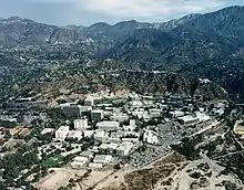 An image featuring a birds-eye, aerial view of the laboratory campus buildings and surrounding landscape. The site is nestled in a valley between green, rolling mountains.