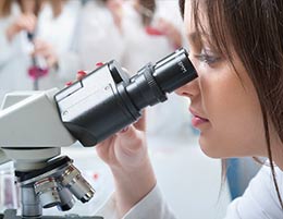 A laboratorian looking at slide under a microscope.