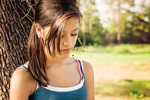 Adolescente que se inclina contra un árbol
