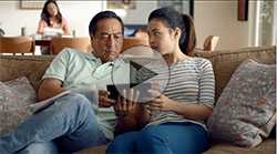 A father and daughter seated on a couch, looking at a tablet screen together