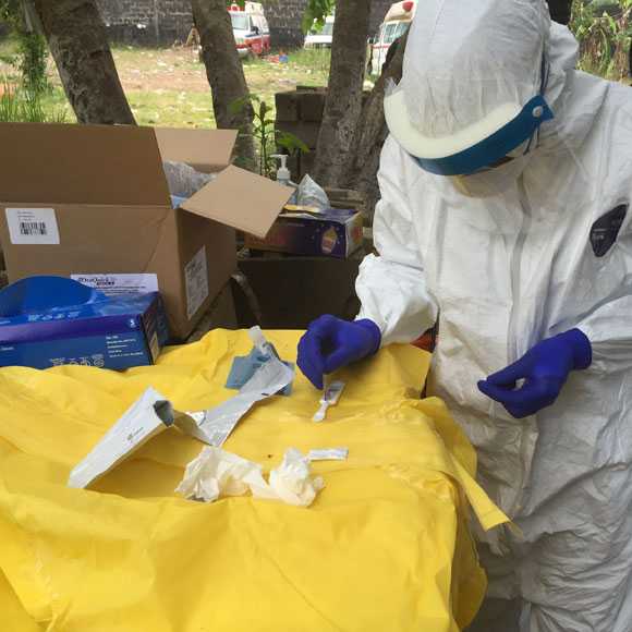 A disease detective wearing protective equipment conducts field testing of samples in Liberia