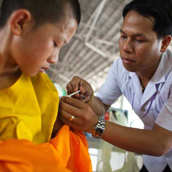 A male nurse giving a vaccine to a young monk in orange robes