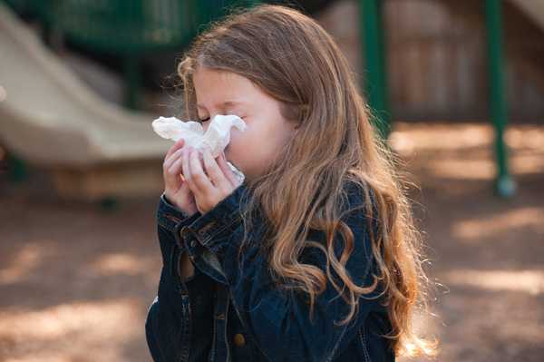 A young girl blowing her nose into a tissue