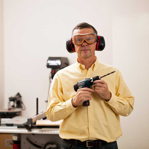 a man in a home workshop holding a drill and wearing ear protection