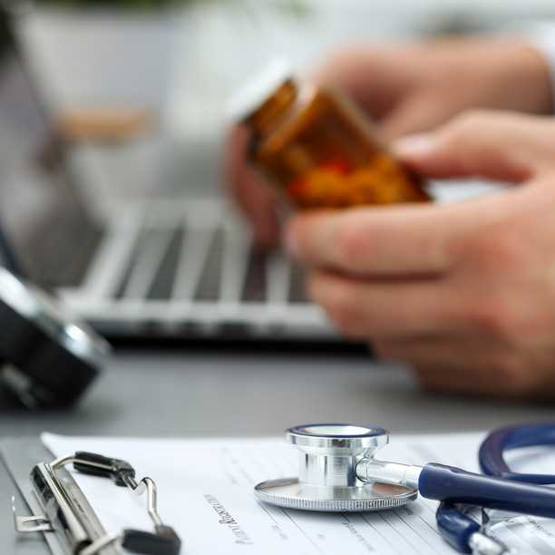 Health care provider using laptop to look up prescription information online. Stethoscope and prescription pad in foreground.