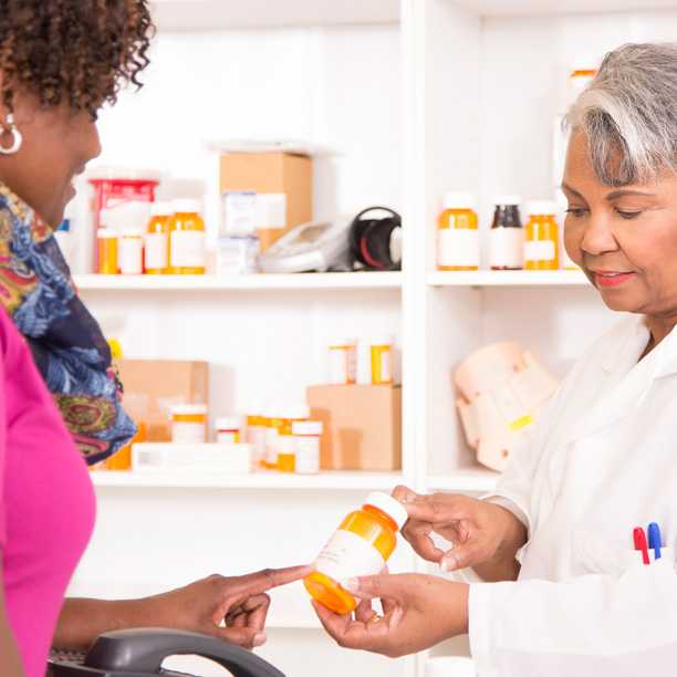 Pharmacist reviewing information on prescription bottle with patient.