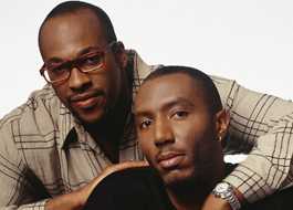 MSM couple posed with one man behind the other and his arm wrapped around and resting on the other man's shoulder