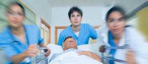 Imagen de tres médicos con batas azules empujando una camilla en la que llevan a un paciente