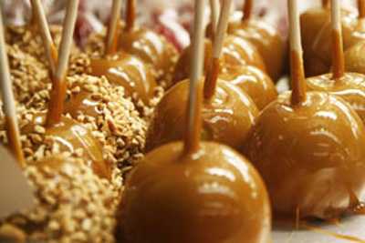 Image shows a tray of shiny caramel apples with and without peanuts