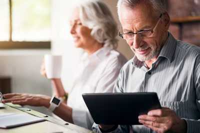 Woman drinking from cup and man using tablet.