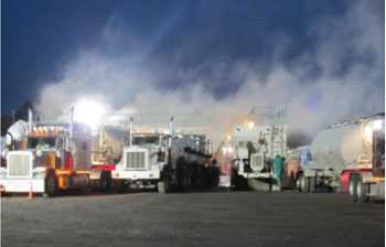 Clouds of dust are visible as sand trucks are unloaded at a hydraulic fracturing site.