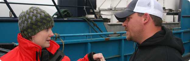 A NIOSH researcher discusses man overboard safety with the skipper of a crab vessel during a survey in Dutch Harbor, AK with the skippers vessel in the background.