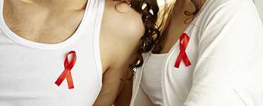 The chests of two individuals wearing red AIDS ribbons.